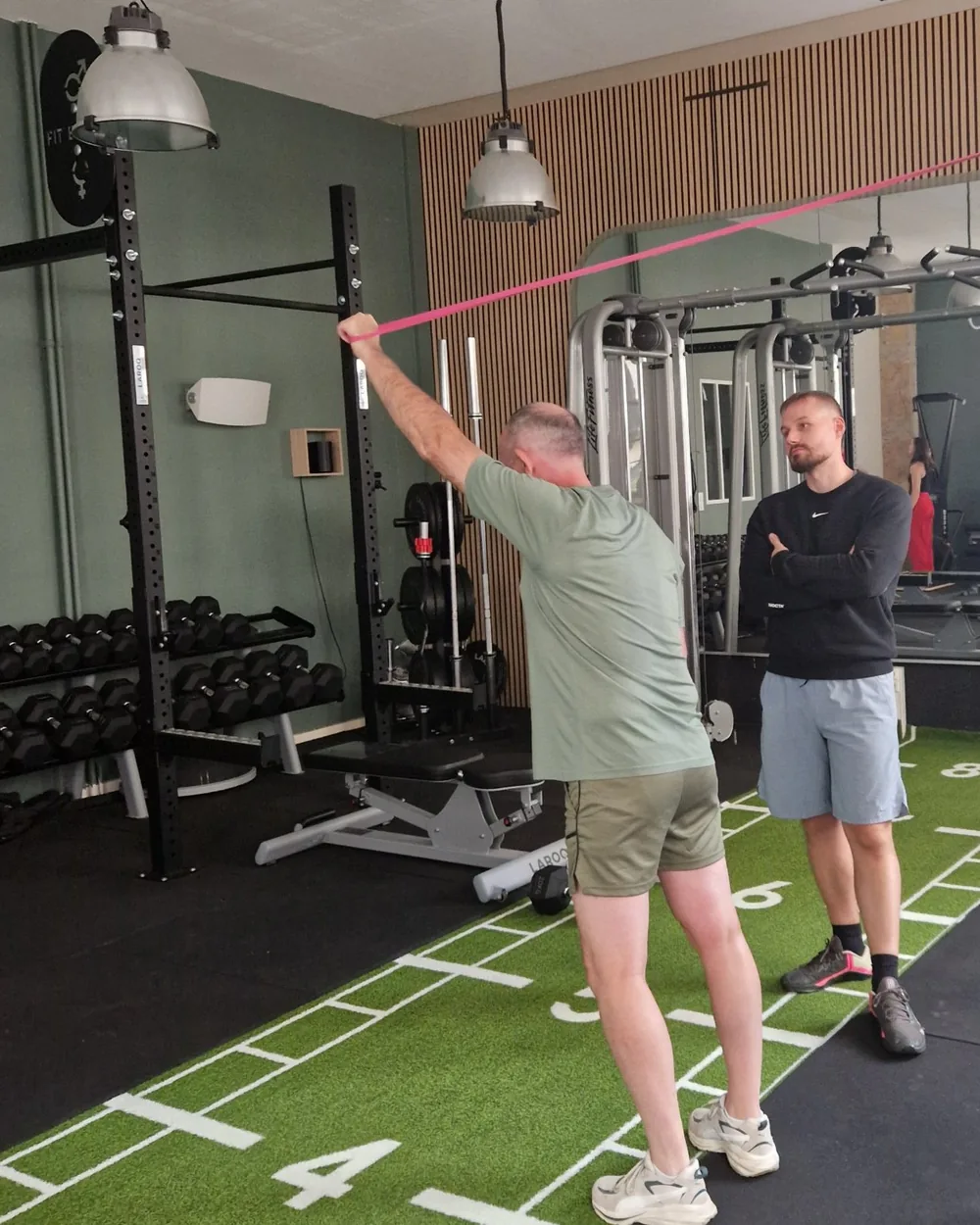 Exercice de renforcement de l'épaule avec un élastique, sous le regard du coach, au studio Top Strength à Lyon 6