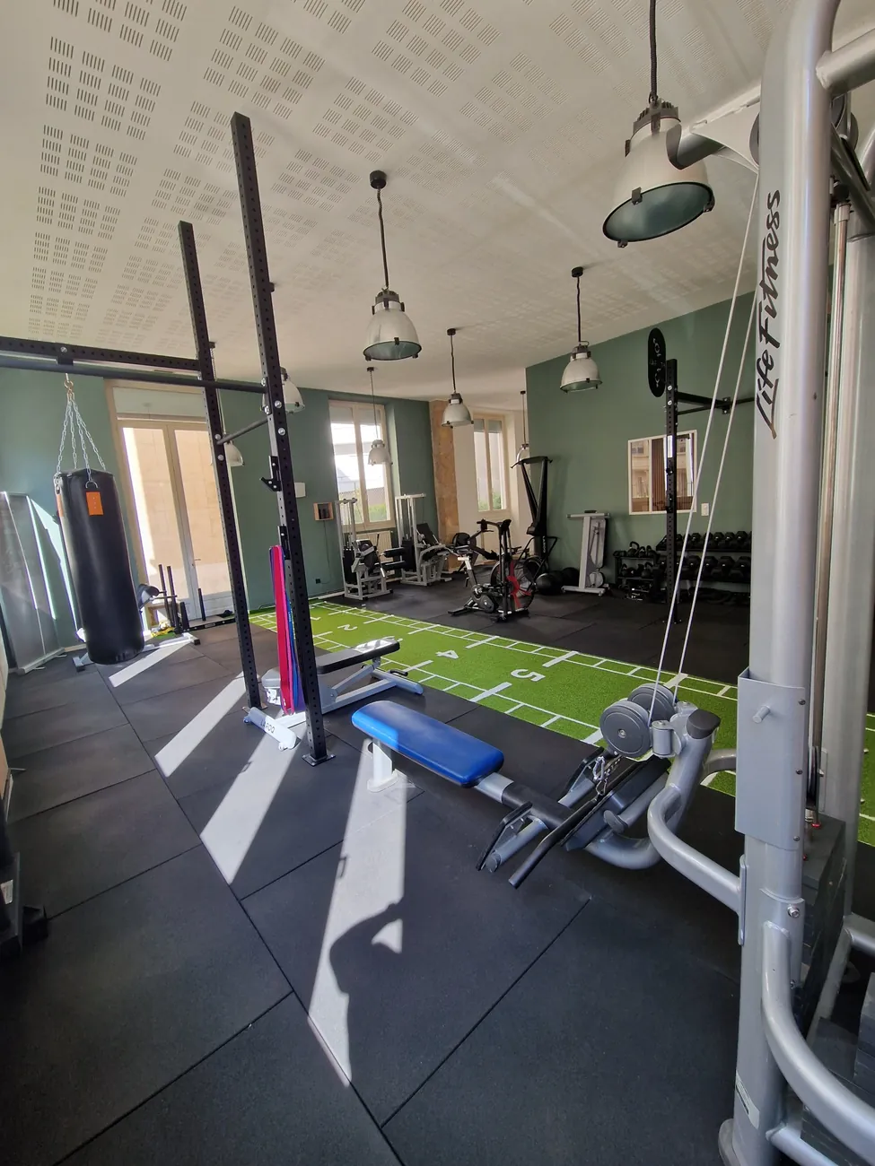 Sac de frappe, bancs et poulies devant les grandes fenêtres du studio Top Strength à Lyon 6